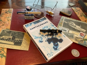 Schreibtisch mit alten Füllern, Tintenfass und dem Buch „Samtschwart“